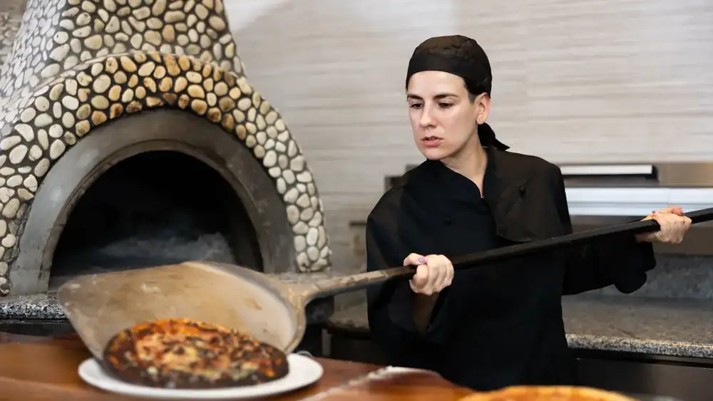 Pizzabäckerin holt eine Pizza aus dem Holzofen
